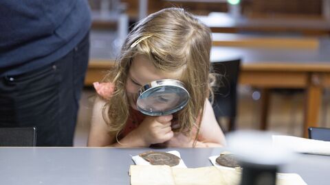 Ein Mädchen schaut sich mit einer Lupe alte Dokumente an.