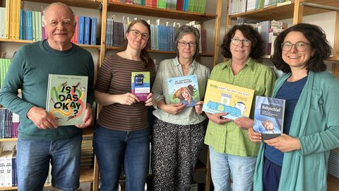 Die Jury würdigte das Engagement und den Mut des Mabuse-Verlags aus Frankfurt, sich Themen zu widmen, die oft jenseits des literarischen Rampenlichts liegen. Mitarbeiter des Mabuse-Verlags stehen mit Büchern vor einem Bücherregal.
