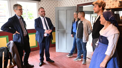 Minister Gremmels steht mit kostümierten Leuten in einem historischen Haus im Hessenpark