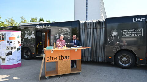 Der „DemokratieWagen“ ist ein 20 Meter langer Linienbus, der als mobiler Erfahrungsraum für eine vielfältige und streitlustige Demokratie auf Frankfurts Straßen unterwegs ist Minister Gremmels steht vor einem großen Bus, dem DemokratieWagen