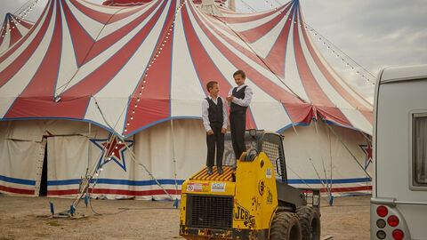 Szene aus "Zirkuskind": Ein Bagger steht vor einem Zirkuszelt.