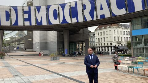 Minister Gremmels steht in Brüssel vor einem Banner mit der Aufschrift "Democracy"
