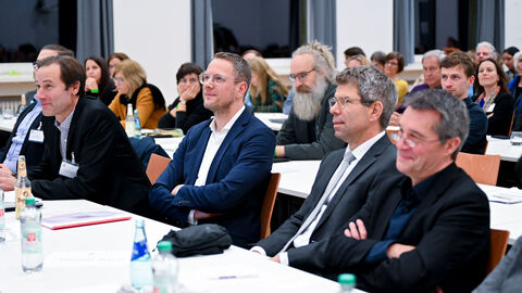 Staatssekretär Degen sitzt am Tisch und lauscht einer Rede.