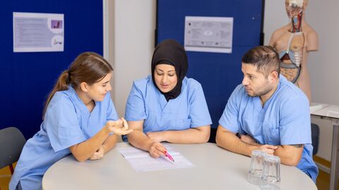Drei junge Menschen in Pflegepersonal-Kleidung sitzen in einer Besprechung.