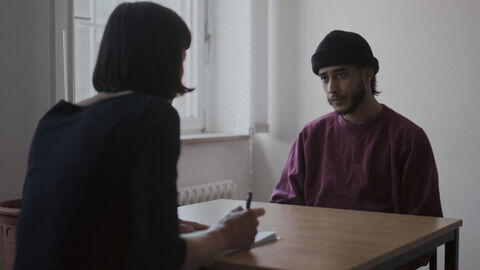 Szene aus "Haus 4": Zwei Personen sitzen am Tisch und unterhalten sich.