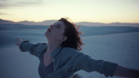 Szene aus "I'll be gone in June": Eine Frau breitet ihre Arme aus und schaut zum Himmel