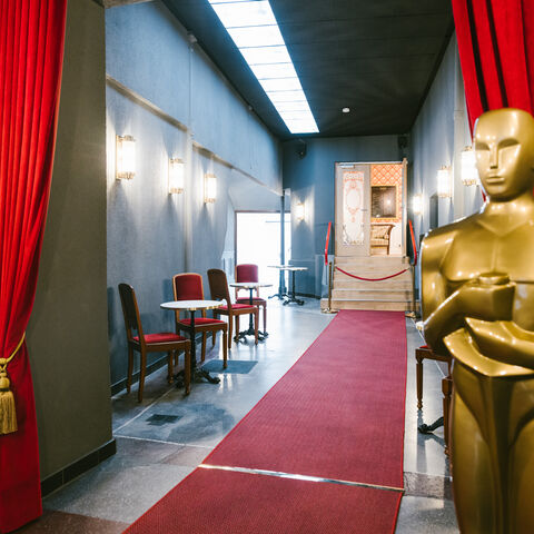 In Kinos können Filme ihre Kraft entfalten, sie sind Orte der Kreativität, des kulturellen Erlebnisses und des Austauschs. Eingang der FilmBühne in Bad Nauheim, man sieht einen Gang mit rotem Teppich, lebensgroßer Oscar-Statue und roten Vorhängen