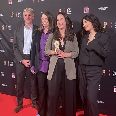 Die Frankfurter Buchmesse vergibt beim Hessischen Film- und Kinopreis den „Preis der Frankfurter Buchmesse für die beste Adaption“. In diesem Jahr wird „Ellbogen“ von Aslı Özarslan ausgezeichnet. Menschen vor einer Fotoleinwand