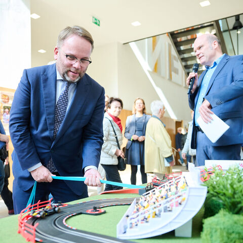 In der hessischen Landesvertretung konnte man Spielzeugautos mit Fitnessbändern bewegen - und dabei etwas über Materialforschung erfahren. Minister Gremmels probiert ein Experiment am Stand aus.